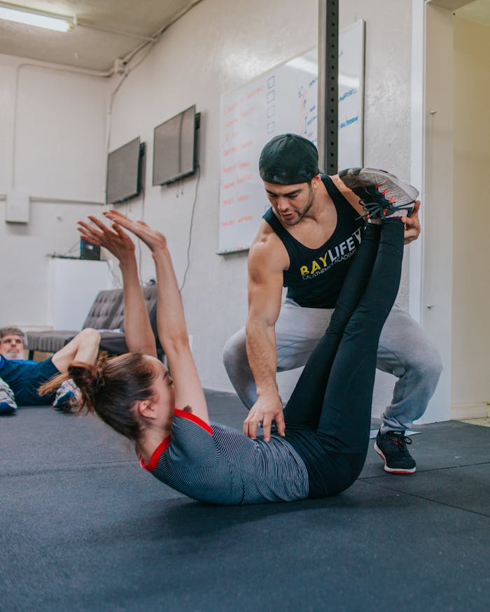 Personal trainer helping a woman with flexibility exercises in a gym setting.
