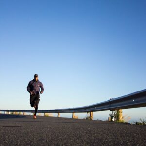 An athletic man jogging on an open road with a clear blue sky in Cape Town, South Africa.